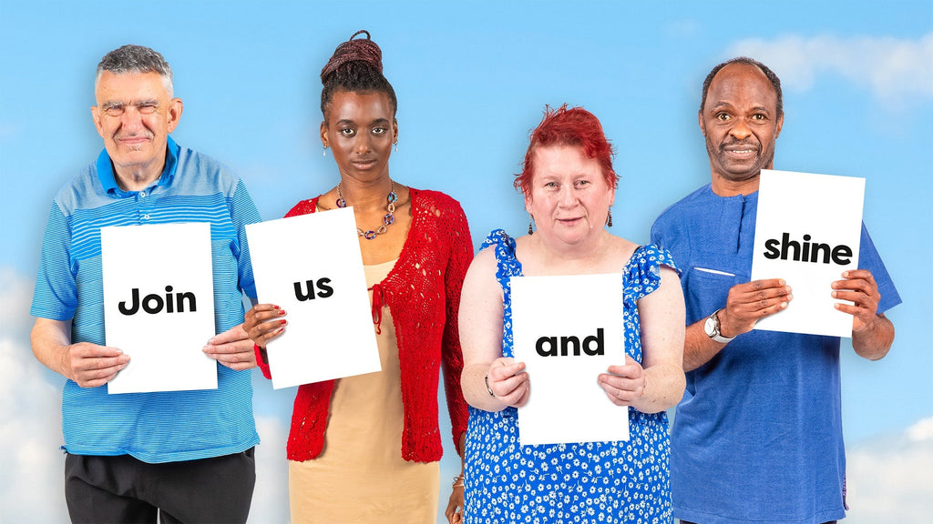 Four individuals stand in front of a bright blue sky with light clouds. Each holds a white sign with bold black text that together reads: ‘Join us and shine.’ They are dressed in colourful clothing, smiling warmly and invitingly.